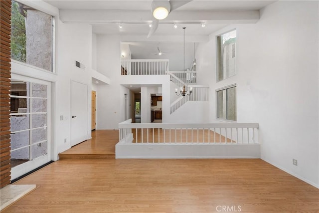 interior space with an inviting chandelier, light hardwood / wood-style floors, beamed ceiling, and a high ceiling