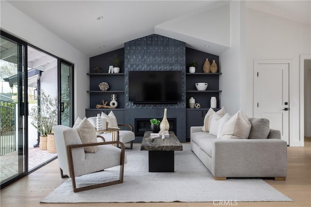 living room featuring a tiled fireplace, vaulted ceiling, and light hardwood / wood-style floors