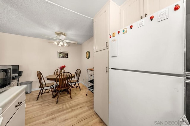 kitchen featuring light wood-type flooring, white cabinets, white refrigerator, ceiling fan, and a textured ceiling