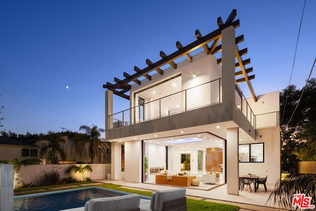 back house at dusk featuring an outdoor living space, a patio area, a fenced in pool, and a balcony