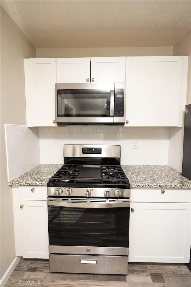 kitchen with appliances with stainless steel finishes, white cabinetry, wood-type flooring, light stone countertops, and decorative backsplash