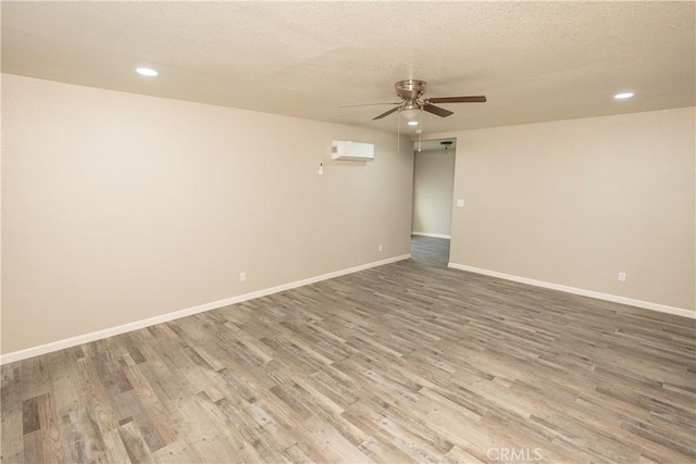 spare room with ceiling fan, wood-type flooring, a wall unit AC, and a textured ceiling