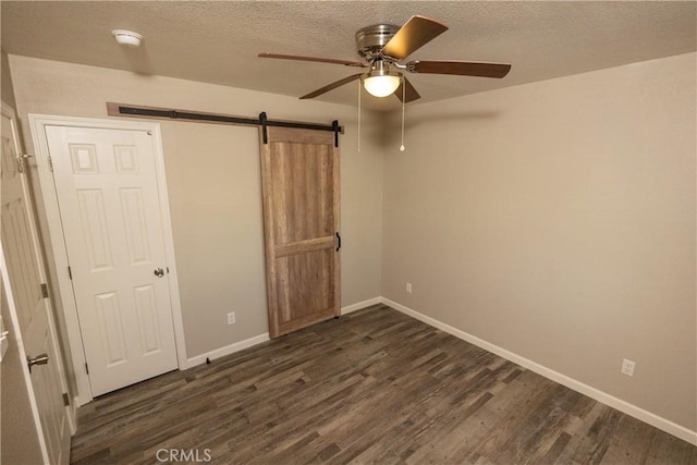 unfurnished bedroom with a barn door, ceiling fan, dark hardwood / wood-style flooring, and a textured ceiling