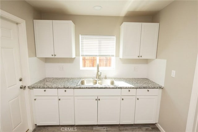 kitchen with white cabinetry, sink, hardwood / wood-style flooring, and light stone countertops