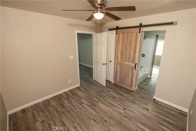 unfurnished bedroom with a barn door, ceiling fan, and dark hardwood / wood-style floors