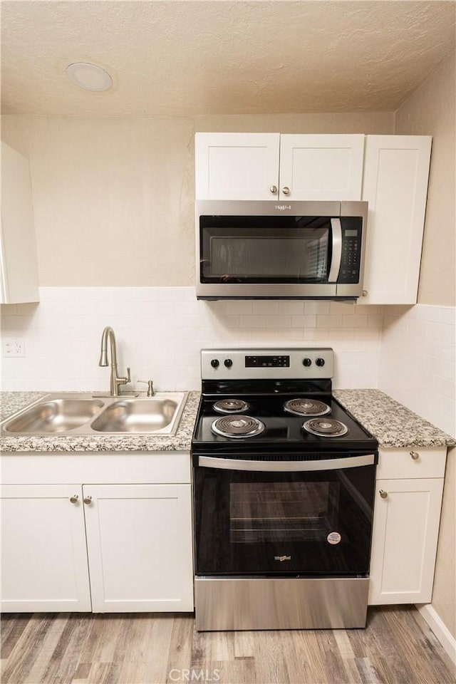 kitchen with appliances with stainless steel finishes, white cabinetry, sink, decorative backsplash, and light hardwood / wood-style flooring