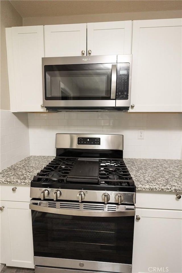 kitchen featuring white cabinetry, appliances with stainless steel finishes, light stone counters, and decorative backsplash