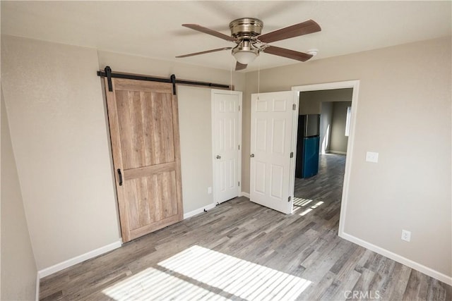 unfurnished bedroom featuring hardwood / wood-style floors, a closet, a barn door, and ceiling fan