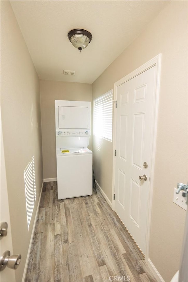 washroom with stacked washing maching and dryer and light wood-type flooring