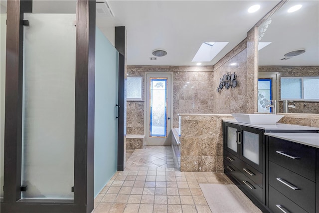 bathroom with vanity, plus walk in shower, a skylight, and tile walls