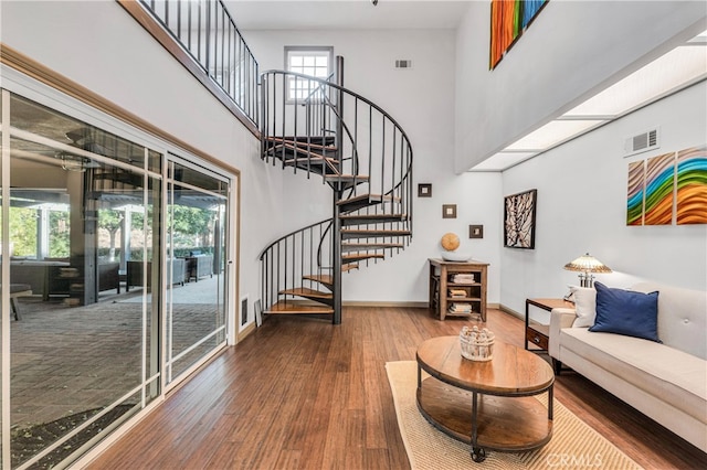 living room featuring a towering ceiling, wood-type flooring, and a skylight