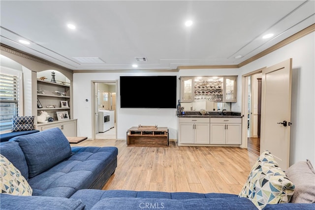 living room with washer / clothes dryer, crown molding, light hardwood / wood-style floors, and indoor wet bar