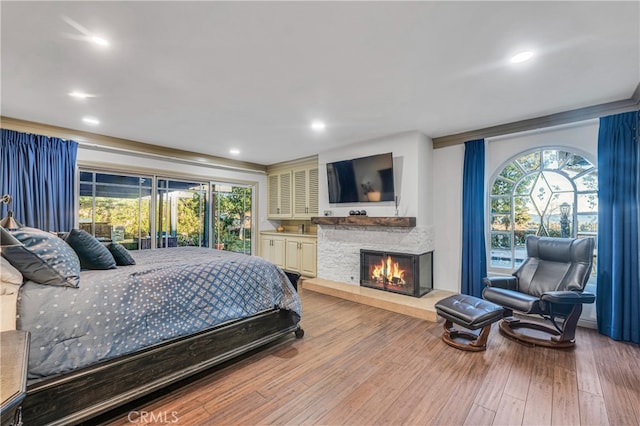 bedroom with multiple windows, a stone fireplace, and hardwood / wood-style floors