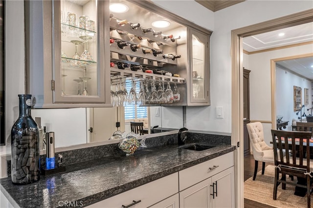 bar featuring sink, white cabinetry, ornamental molding, hardwood / wood-style flooring, and dark stone counters