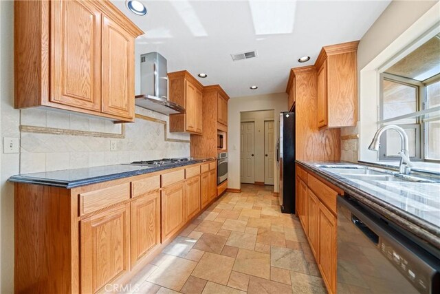 kitchen featuring appliances with stainless steel finishes, a skylight, tasteful backsplash, sink, and wall chimney range hood