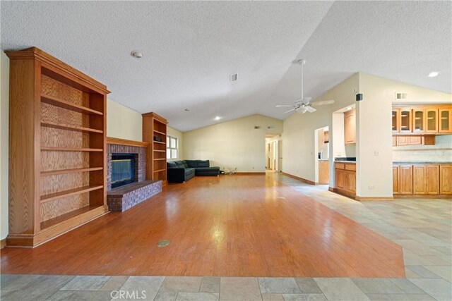 unfurnished living room with vaulted ceiling, a textured ceiling, a brick fireplace, light hardwood / wood-style flooring, and ceiling fan