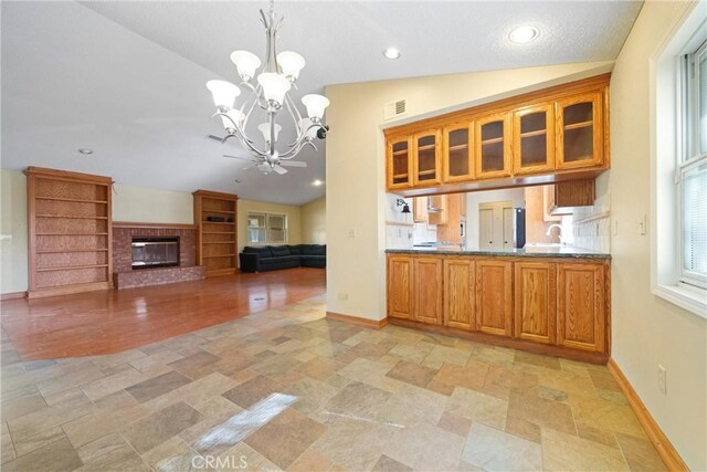 kitchen with a chandelier, vaulted ceiling, a brick fireplace, hanging light fixtures, and light stone countertops