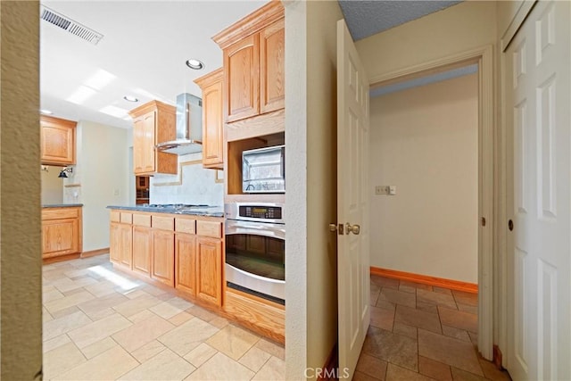 kitchen with light brown cabinetry, wall chimney range hood, tasteful backsplash, and stainless steel appliances