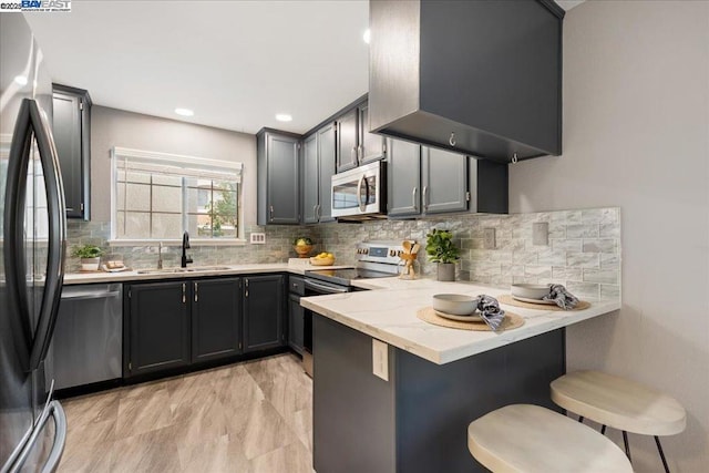 kitchen with appliances with stainless steel finishes, a breakfast bar, sink, light stone counters, and kitchen peninsula