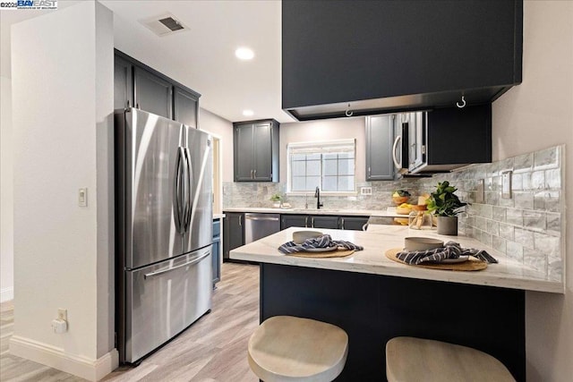 kitchen with a breakfast bar, tasteful backsplash, light wood-type flooring, kitchen peninsula, and stainless steel appliances