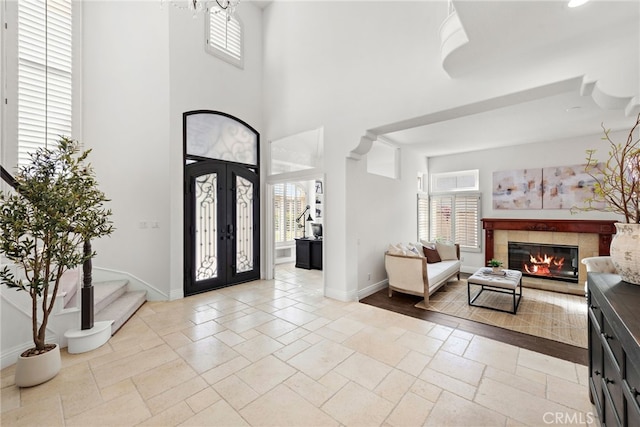 entrance foyer featuring french doors, a towering ceiling, a healthy amount of sunlight, and a fireplace