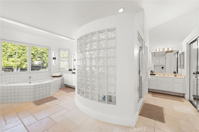 bathroom with a relaxing tiled tub, lofted ceiling, and vanity