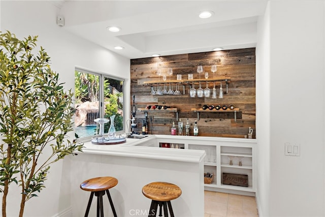 bar with light tile patterned flooring, wooden walls, and sink