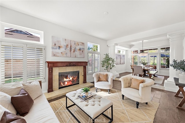 living room with decorative columns, a tiled fireplace, and wood-type flooring