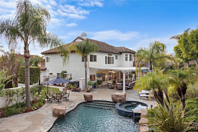 rear view of property featuring a swimming pool with hot tub and a patio area