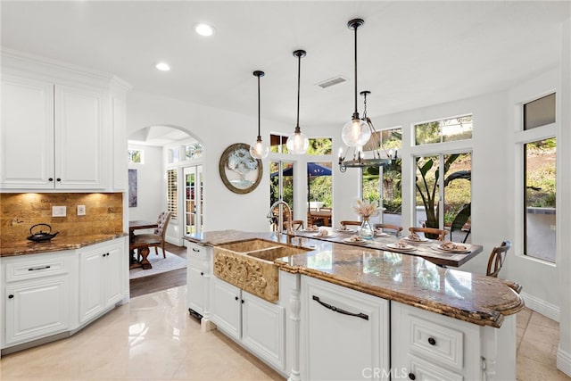 kitchen featuring dark stone counters, sink, a kitchen island with sink, and decorative backsplash