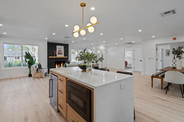 kitchen featuring pendant lighting, light brown cabinetry, black microwave, wine cooler, and light wood-type flooring