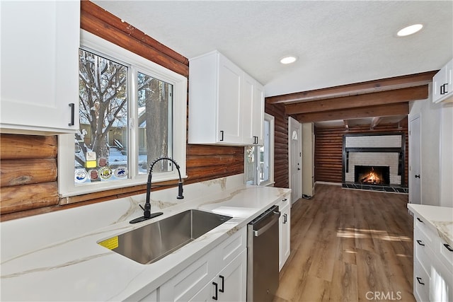 kitchen with white cabinetry, dishwasher, a brick fireplace, and sink