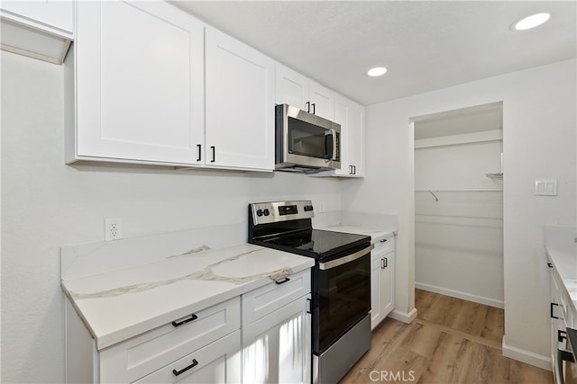 kitchen with white cabinetry, appliances with stainless steel finishes, light stone counters, and light wood-type flooring