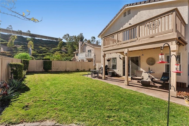 rear view of property with a balcony, a yard, and a patio area