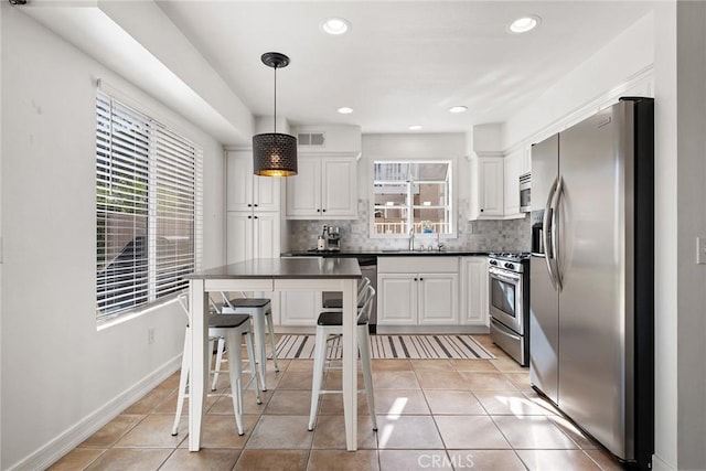 kitchen with stainless steel appliances, decorative light fixtures, light tile patterned floors, and white cabinets