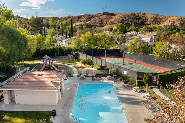 view of swimming pool featuring a playground, a mountain view, and tennis court