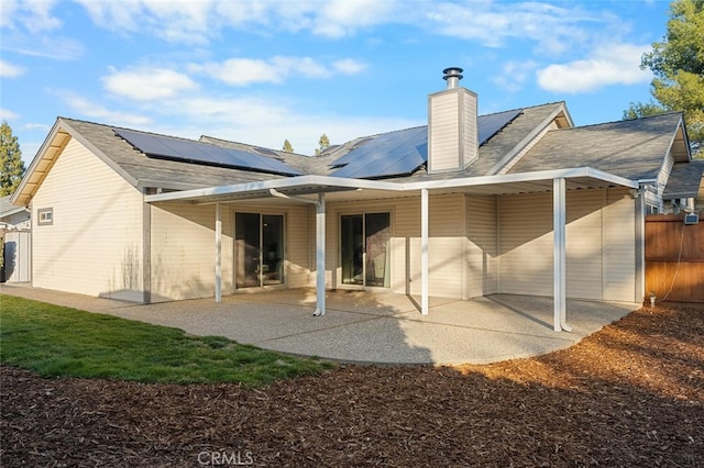 back of property with a chimney, fence, solar panels, and a patio