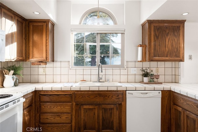 kitchen with tasteful backsplash, tile counters, brown cabinetry, a sink, and white appliances