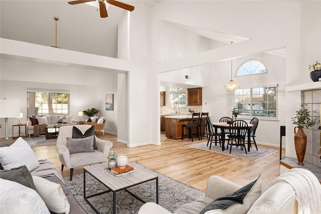 living room featuring high vaulted ceiling, a ceiling fan, light wood-style flooring, and baseboards