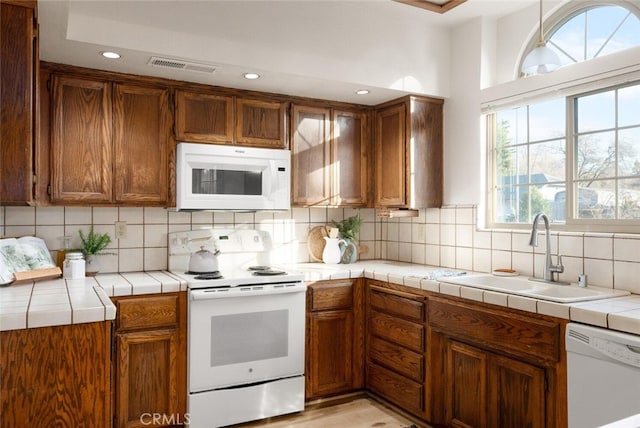 kitchen featuring white appliances, visible vents, tile counters, a sink, and backsplash