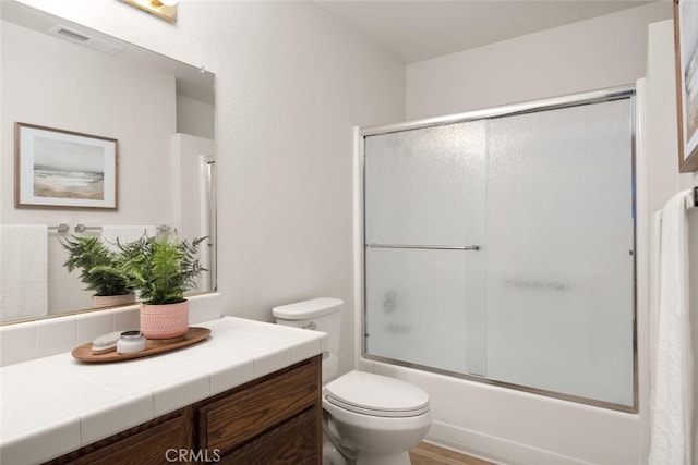 full bath with visible vents, vanity, toilet, and combined bath / shower with glass door