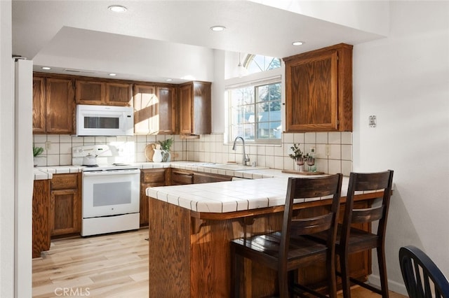 kitchen with tile counters, tasteful backsplash, a sink, white appliances, and a peninsula