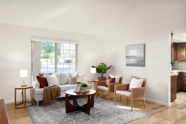 living room featuring baseboards, vaulted ceiling, and light wood-style floors