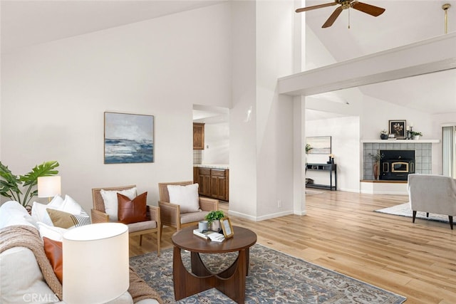 living area featuring light wood-style floors, ceiling fan, high vaulted ceiling, and baseboards