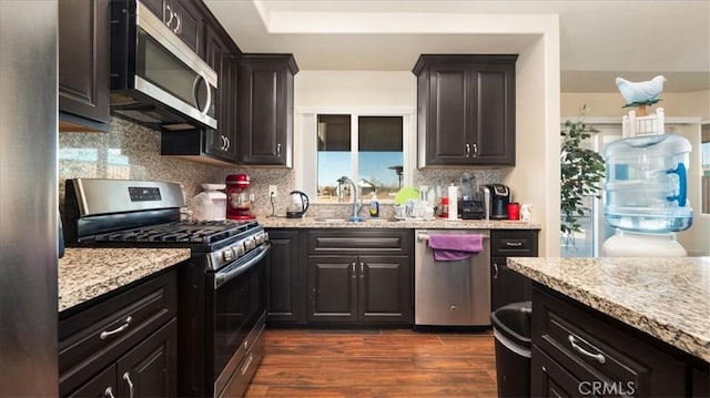 kitchen featuring appliances with stainless steel finishes, dark hardwood / wood-style floors, tasteful backsplash, sink, and light stone counters