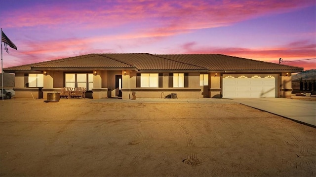 view of front facade featuring a tile roof, a garage, driveway, and stucco siding