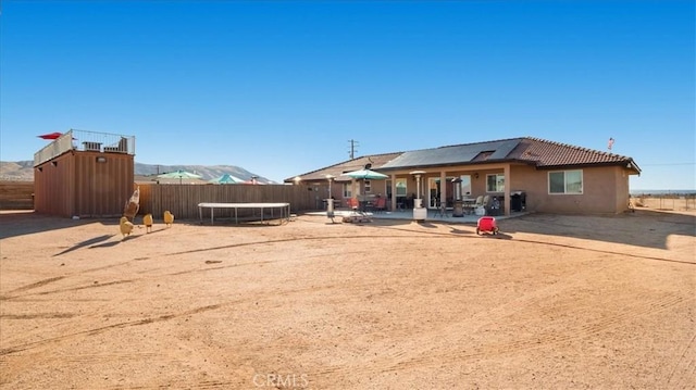 back of house with a mountain view, a trampoline, and a patio area