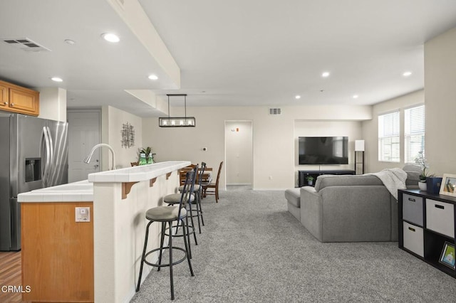 kitchen with a center island, light carpet, stainless steel fridge with ice dispenser, decorative light fixtures, and tile countertops