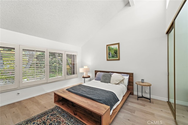 bedroom with light hardwood / wood-style flooring, high vaulted ceiling, a closet, and a textured ceiling