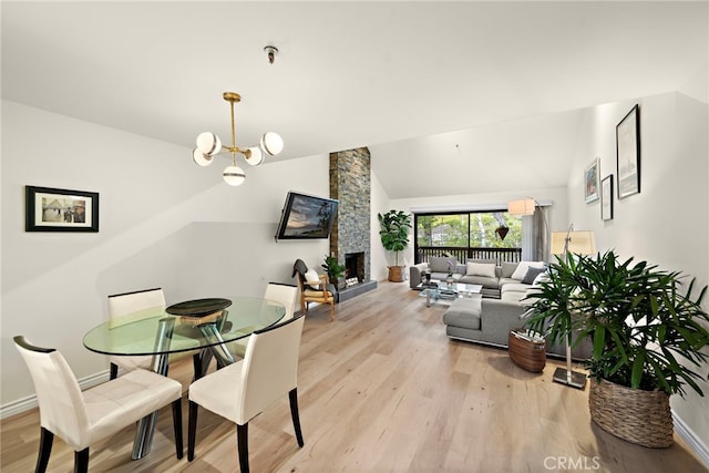 dining room featuring a notable chandelier, light wood finished floors, vaulted ceiling, a stone fireplace, and baseboards